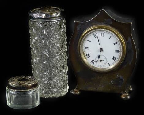 A George V silver travelling clock, the white enamel dial with Roman numerals, on ball feet, Birmingham 1913 and two dressing table jars. (3)