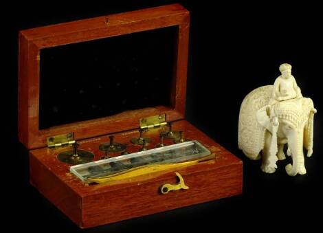 A late 19th/early 20thC Indian ivory carving, in the form of gentleman seated on elephant, 5cm L, and a set of miniature weights in a fitted mahogany case.