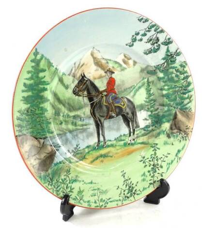 A Royal Staffordshire Clarice Cliff plate, from The Confederation Series of Canada, printed with a Canadian Mountie on horseback, within a river landscape etc., 27cm dia.