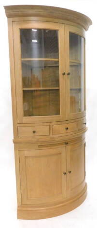 A light oak corner cabinet, the top with a moulded cornice, with two glazed doors enclosing glass shelves above three small drawers, the base with a slide and two panelled doors on a plinth, 209cm H, 110cm W.