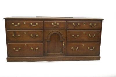 An 18thC oak dresser base, with plain top and an arrangement of central drawer over arch top moulded panel door, enclosed by a bank of three drawers to each side, with brass swan neck handles and oval escutcheons on plinth, 84cm serving height, 180cm W,