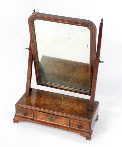 A George II walnut dressing table mirror, with rectangular plate within a moulded frame, on slender tapered square supports, the figured walnut base fitted with three carvetto drawers having walnut linings and with cross banding, raised upon ogee bracket