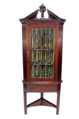 A George III mahogany standing corner cabinet with a broken arch Greek key moulded cornice, having central rococo cameo finial over a single astragal glazed door, revealing shaped shelved interior enclosed by channel sides, the door having pierced brass e