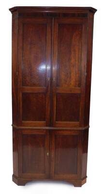 A George III tall standing corner cupboard, with canted sides and plain moulded cornice and frieze, with three serpentine shaped shelves to the upper cabinet and enclosed with panelled doors, having ivory escutcheons, on low bracket feet, 228cm H, 106cm W