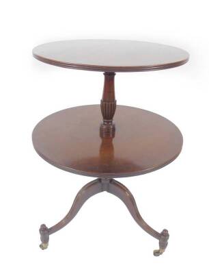 A Regency mahogany two tier graduated circular dumb waiter, with reeded edges and turned and semi fluted slender column, the tripod base of slightly haunched slender tapered legs and peg feet raised upon brass cups and castors, 95cm H, largest tier 66cm D