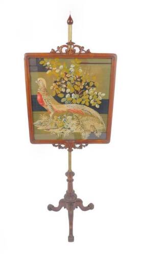 A Victorian mahogany framed pole screen, of rectangular design and with a carved and pierced foliate scroll crest, containing a wool needlework panel depicting a golden pheasant amid foliage, on a brass pole and carved tripod stand carved with acanthus le