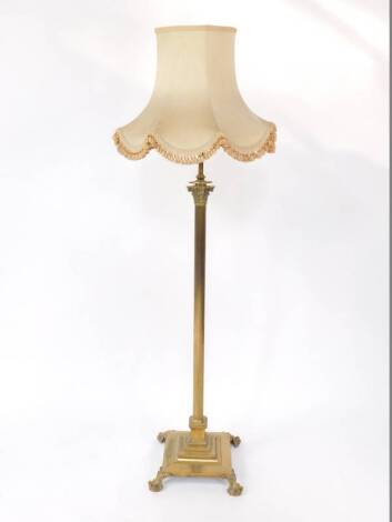 An early 20thC brass standard lamp, of Corinthian column design raised on a stepped square base on four claw feet, fitted for electricity, with tasseled silk shade.