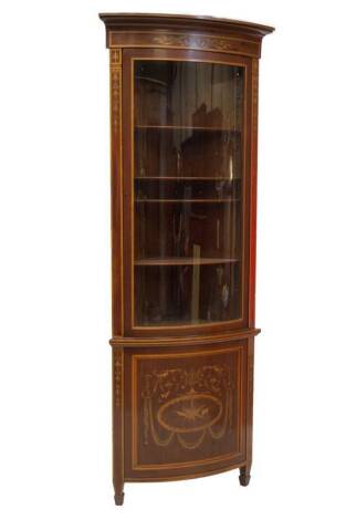 A late Victorian Sheraton revival bowfront standing corner cabinet, with moulded cornice, with a stylised frieze with floral trailing marquetry set in satinwood, box and harewood, over a bowfront glass door with adjustable shelves, enclosed by uprights of