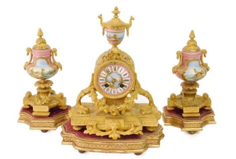 A 19thC gilt metal clock garniture comprising mantel clock of 9cm Dia. enamelled Roman numeric dial centre surmounted by an urn in a classical case set with garlands, masks and flower heads, revealing an eight day movement and flanked by two urn garniture