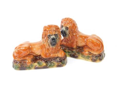 A mid 19thC pair of Bowness pottery figures of lions, modelled in recumbent pose, with glass eyes, on a naturalistic oval base, 25cm H, 33cm W.