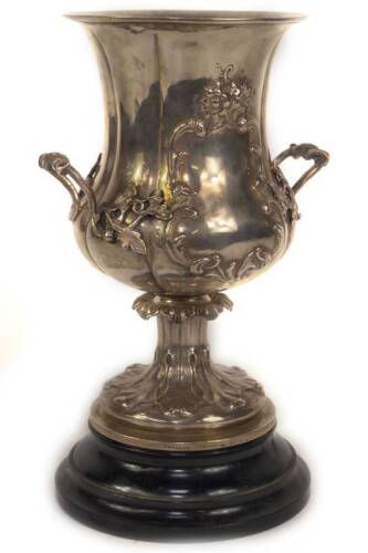 A Victorian campana shaped silver two handled prize cup, with moulded everted rim and repousse scroll decoration incorporating two blank cartouches, with applied foliate and twisted branch handles, raised on a tapered lappet leaf collared stem and circula