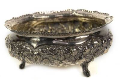 A late Victorian circular silver bowl, with 'crimped' scroll everted border and profusely decorated with repousse fruit and flower head designs, with a blank cartouche, and raised upon three pierced foliate scroll feet, Sheffield 1895, makers Atkin Bros,