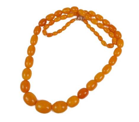 A butterscotch amber beaded necklace, with graduated oblong beads, the largest 2.8cm wide, the smallest 1cm wide, on white string, with yellow metal clasp, unmarked, 90cm long overall, 86.6g all in.