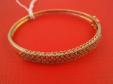 A hinged bangle, the top set with bands of tiny white and fancy cinnamon