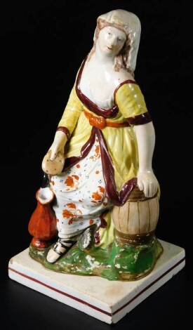 A 19thC Staffordshire pottery figure The Widow, holding a loaf of bread while resting her arm on a barrel, on a square base, c1830, 24cm H.