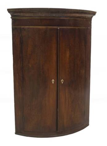 A George III mahogany hanging bowfront corner cupboard, with moulded cornice over two doors, with reeded base, 104cm H.