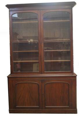 A Victorian mahogany cabinet bookcase, with moulded overhang cornice over two arch moulded and glazed doors, revealing adjustable shelves with mahogany fronts over two arch moulded panel doors, revealing two drawers over shelf and covered base on plinth,