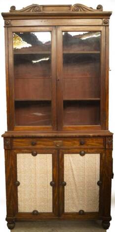 A William IV walnut cabinet bookcase, with scroll carved and moulded frieze with roundels, over two glazed doors revealing adjustable shelves, over a single oak lined frieze drawer with brass knob handles, over two panel doors with fabric panels, on turne