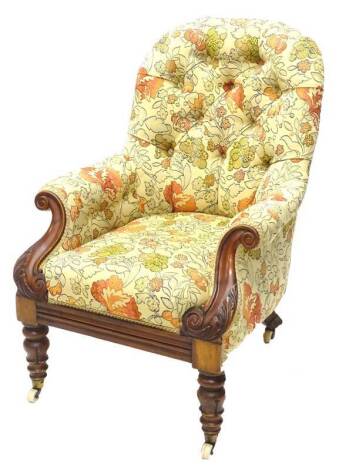 A Victorian mahogany armchair, upholstered in brightly coloured floral fabric, the leaf carved arm supports on turned and lappet tapering legs with ceramic castors.