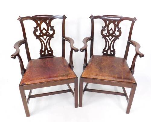 A pair of late 19thC mahogany carver chairs in the Chippendale manner, with scrolling ribbon backs and drop in red leather seats, on square legs and plain stretchers.