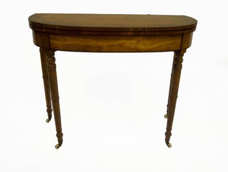 A George III satinwood card table, with rounded rectangular rosewood crossbanded folding top, frieze with ebony stringing on ringed turned taper legs with brass cup and ceramic castors, 72cm H, 90cm W, 45cm D when closed.