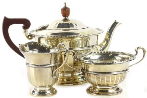 A George V silver three piece tea set, with a part faceted body, gadrooned border, the teapot with composition handle and knop, Birmingham 1931, 19¾oz gross.