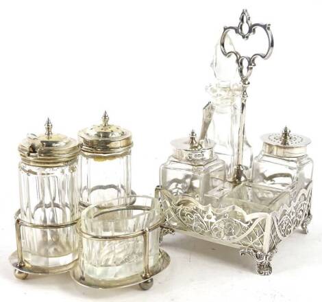 A George V silver four bottle cruet, with pierced sides and handle, some glass jars with silver mounts and a trefoil shaped similar example. (2)