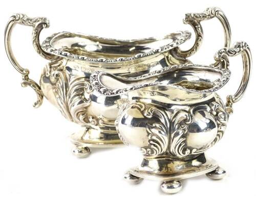 An Edwardian two handled silver sugar bowl, with embossed decoration of scrolls, etc., shaped handles and bun feet, and a matching milk jug, Chester 1903, 10½oz, (2).