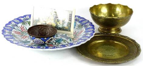 Various continental items, to include a modern Iznik charger, middle eastern enamel bowl, a brass plate and bowl with repousse decoration in the Islamic style and a middle eastern painting depicting a lady various figures within a building in bleached bon