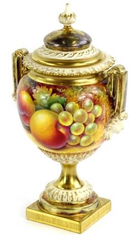 A Royal Worcester porcelain two handled urn and cover, painted with fruit by Paul English, the lid with a tapering finial, the base decorated with female masks, leaves etc., on a square foot, painted marks in black to underside and numbered 2363, in prese