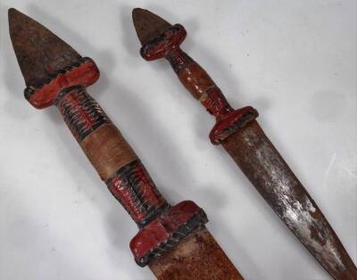 A 20thC African tribal knife and scabbard, probably Nigerian, with metal shaped end and turned handle, 56cm W, and another similar, but smaller. (2) - 2