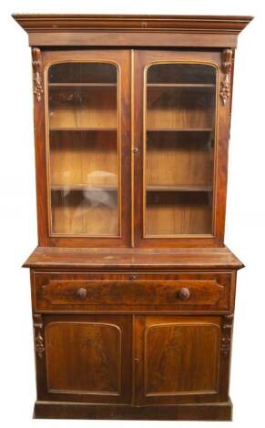 An early Victorian mahogany secretaire cabinet bookcase, with moulded cornice, scroll and floral carved support doors, with arched glazed panels and adjustable shelves, the secretaire drawer having writing slope, pigeon holes and oak drawers, with mahogan