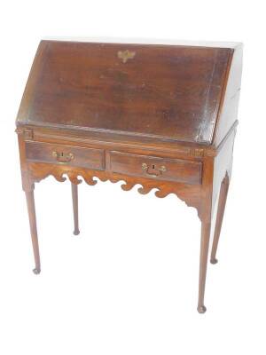 A George II oak bureau on stand, the fall flap opening to reveal an inlaid central door, flanked by four recesses above six short and one long drawer, the stand with two frieze drawers over and a shaped apron, raised on turned tapering legs and pad feet,