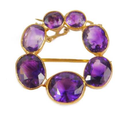 An amethyst circular brooch, set with varying sized amethyst stones, mainly oval cut, the largest stone 11mm wide, the smallest 6mm wide, in rub over setting, with pierced sides and single pin back, with safety chain, yellow metal, unmarked, possibly 18ct