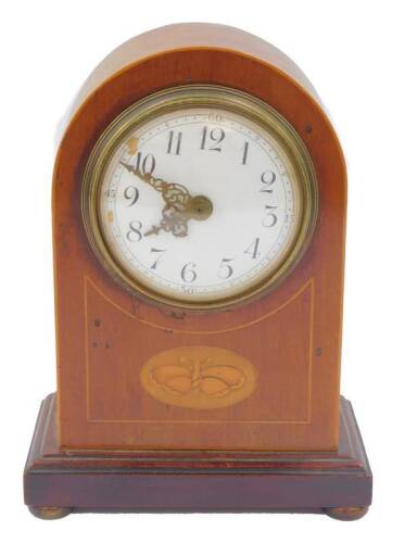 An Edwardian mahogany mantel clock, with butterfly and line inlay, circular enamel dial, bearing Arabic numerals, clockwork movement, the case of domed formed, raised on stepped rectangular base, on brass bun feet, with key, 21cm H.