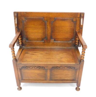 An early 20thC oak monks bench, with a plain top and panelled back, arms with bobbin turned supports, the seat with a panelled front, raised on square supports and turned feet, 92cm H, 91cm W, 45cm D.