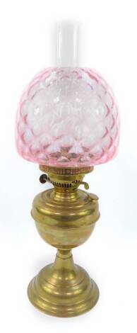 An early 20thC brass oil lamp, with a glass chimney and pink honeycomb glass shade, 53cm H.