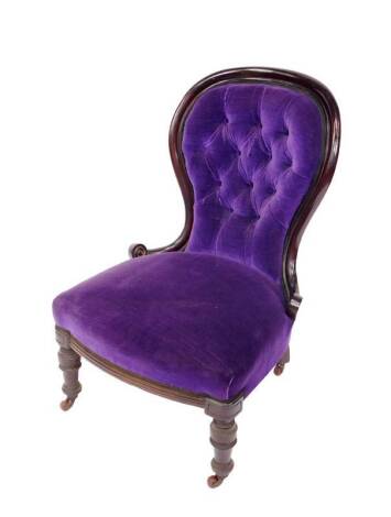 A Victorian mahogany balloon back nursing chair, upholstered in button back purple draylon and overstuffed seat cover, raised on turned legs, on castors.