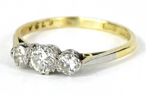 A three stone diamond ring, set with three round brilliant cut diamonds, in claw setting, with pierced ring head, set in platinum on a yellow metal band, ring size P½, 2.5g all in.