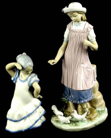 A Lladro porcelain figure, of a lady wearing a purple pinafore, feeding some doves, printed mark in blue to underside, 28cm H, and a Spanish porcelain figure of a dancing girl. (2)