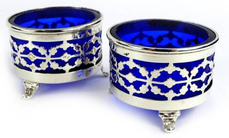 A pair of George V silver cylindrical salts, each with pierced decoration, blue glass liner and tapering feet, Chester 1911