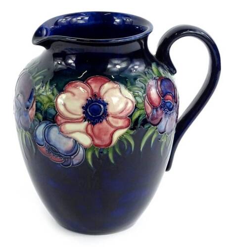 A Moorcroft pottery jug, decorated with a band of anemones on a navy blue ground, impressed and hand written marks to underside, handle restored, 20cm H.