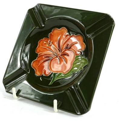 A Moorcroft pottery ashtray, decorated with an orange flower on a dark green ground, impressed marks to underside, 12cm W,