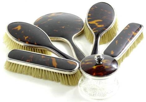 A George V silver and tortoiseshell backed dressing table set, comprising two hair brushes, 23cm W, two clothes brushes, a lidded jar and hand mirror, Birmingham 1922, (6).