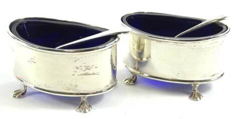 A pair of George V silver salts, of oval form on quadruple hairy paw feet, with blue glass liners, Birmingham 1912, 6cm W, with associated spoons, 1oz.