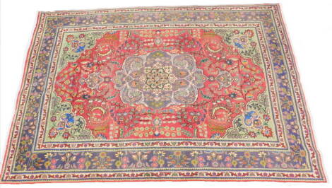 A Persian design rug, with a central medallion in grey, with a red field decorated with leaves, flowers etc., green spandrels with one wide and two narrow borders, 286cm x 195cm.