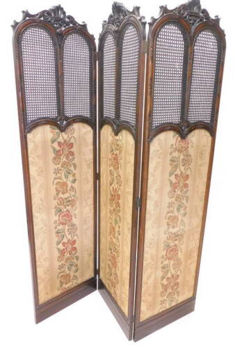 An early 20thC mahogany three fold screen, each with a pierced scroll and crown carved crest above a double caned panel and a fabric panel, on a plinth, 186cm H, 150cm W.