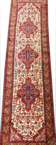 A Persian runner, with a design of three medallions in red and navy on a cream ground with one wide and two narrow borders, 320cm x 88cm.
