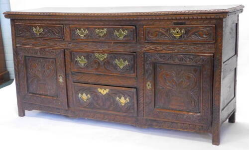 A 19thC oak dresser base, carved overall with scrolls etc., with an arrangement of five drawers and two panel doors on stiles, 161cm W.