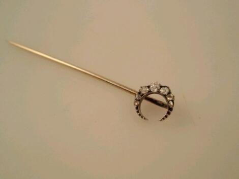 A stick pin in yellow metal topped with a graduated tiny diamond set crescent